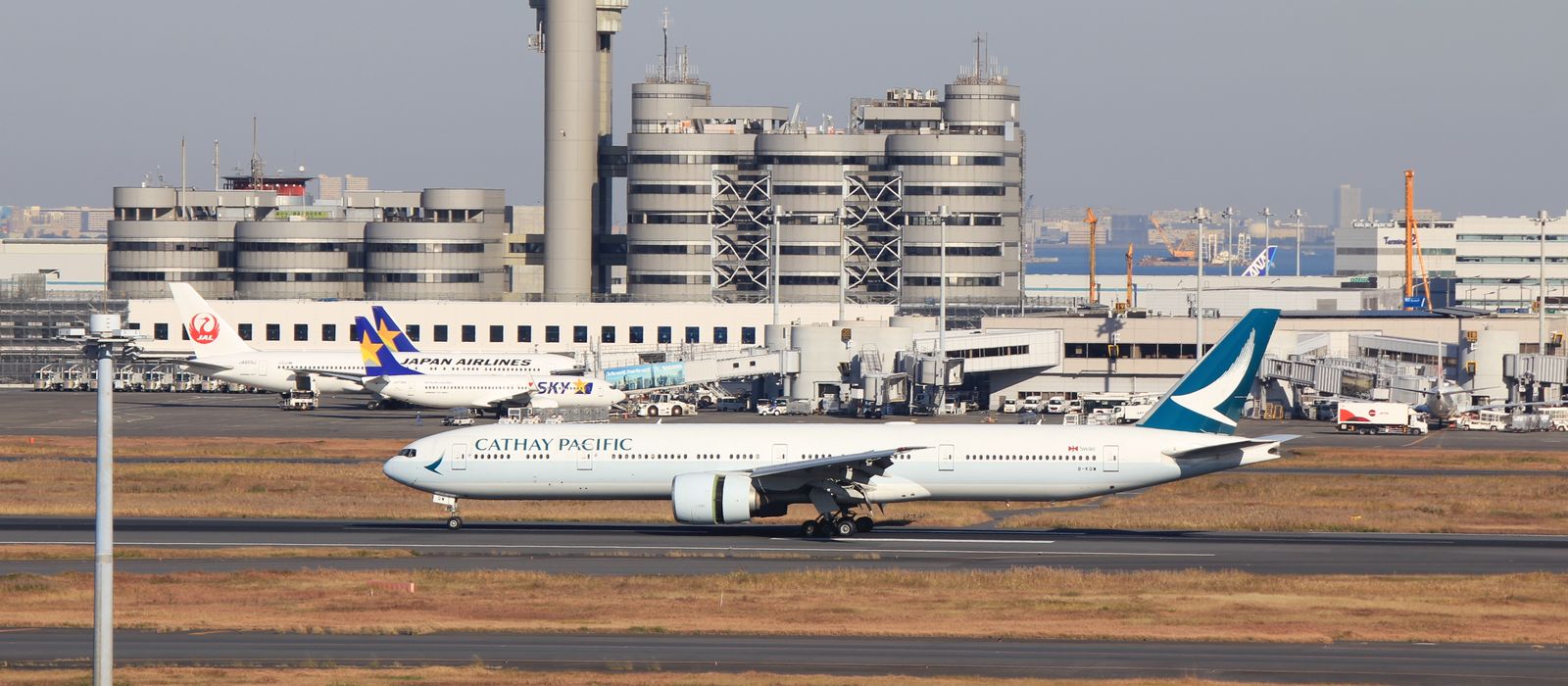 Cathay Pacific plane on runway at Narita Airport, Tokyo, with terminal and control tower in view.