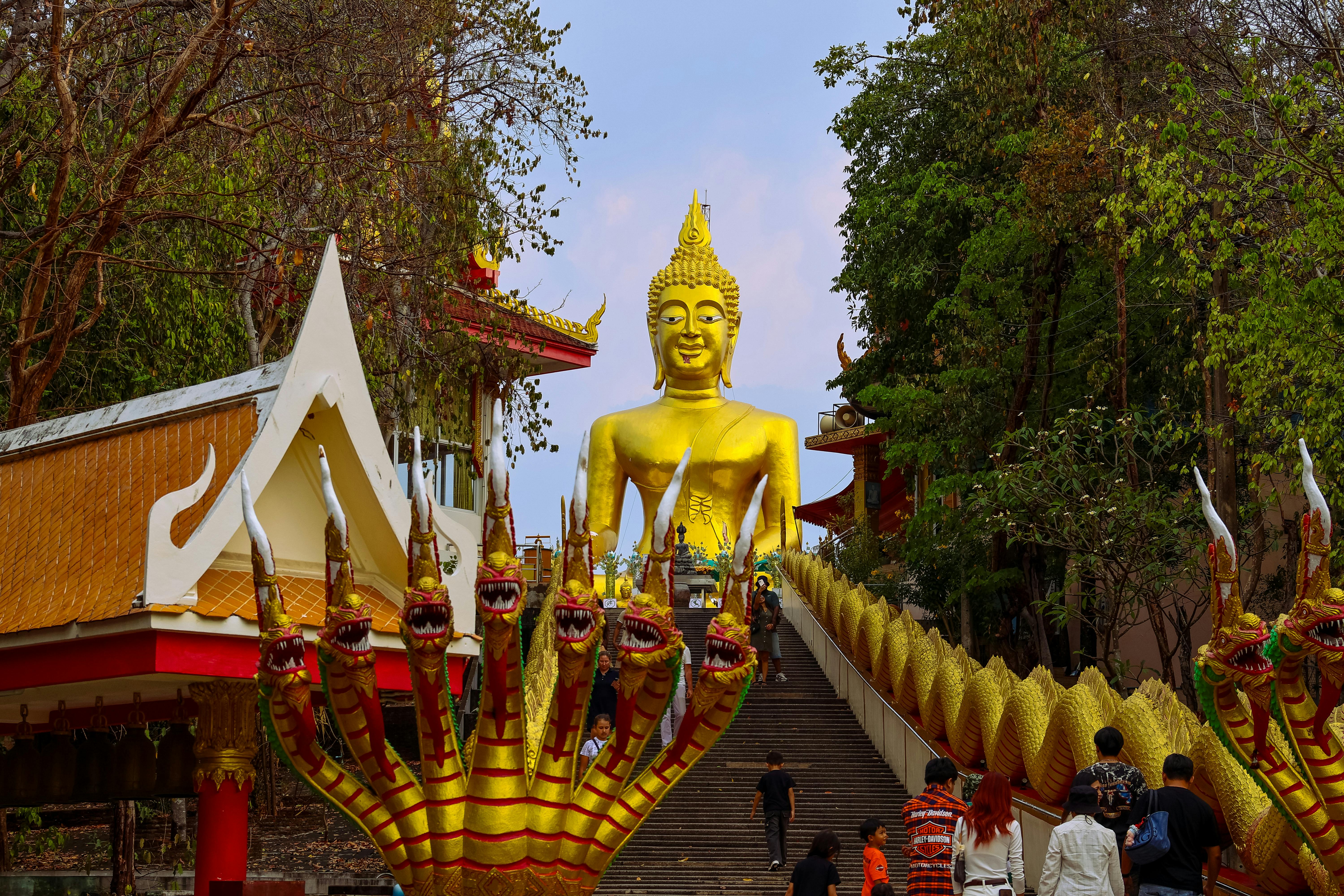 Visitors climbing stairs to a golden Buddha statue at a vibrant Thai temple.