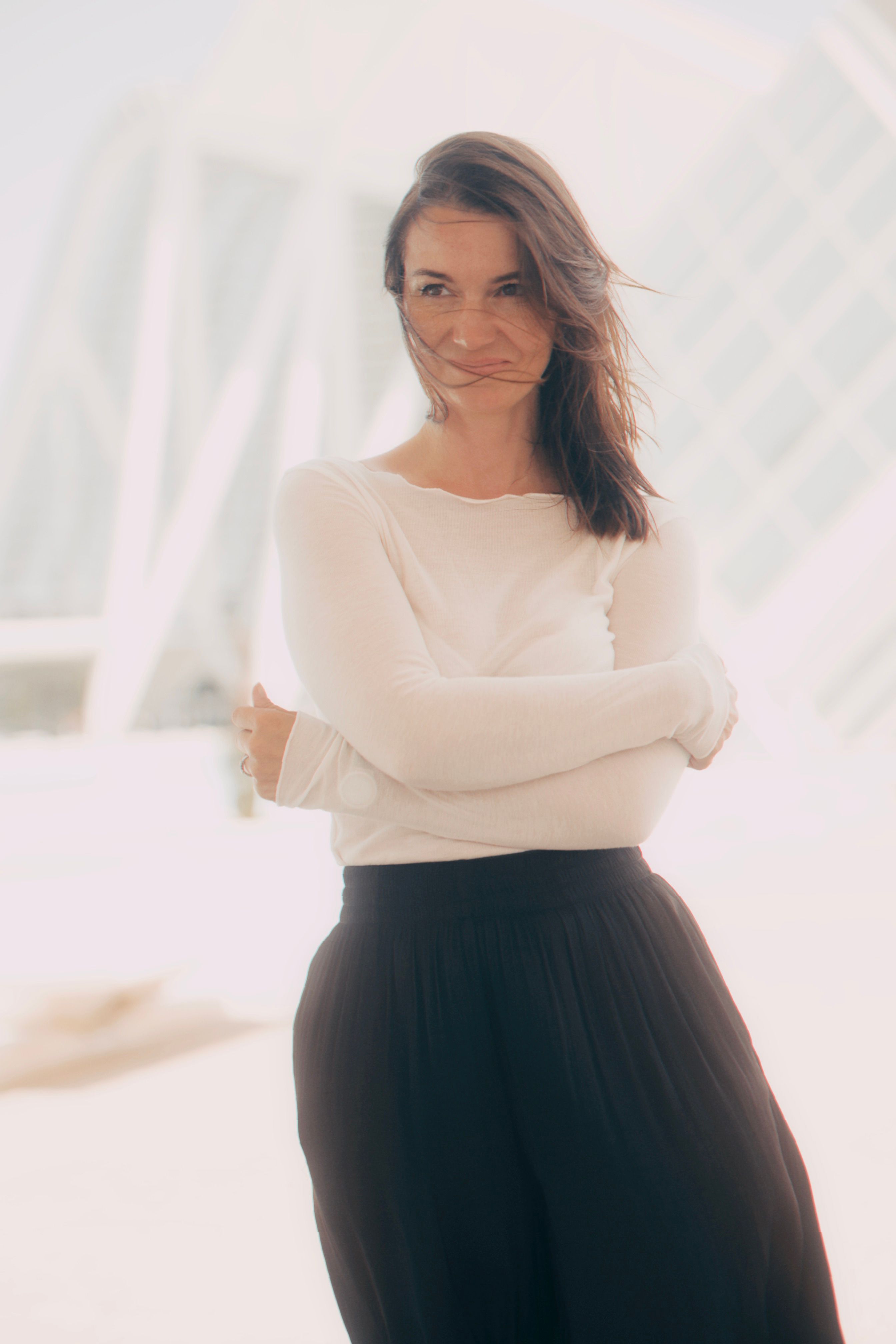 Confident woman with arms crossed in sunny outdoor setting, conveying elegance and poise.