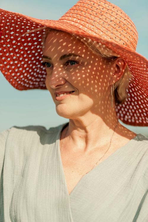 Free A woman smiles peacefully while wearing a wide-brimmed straw hat outdoors on a sunny day. Stock Photo