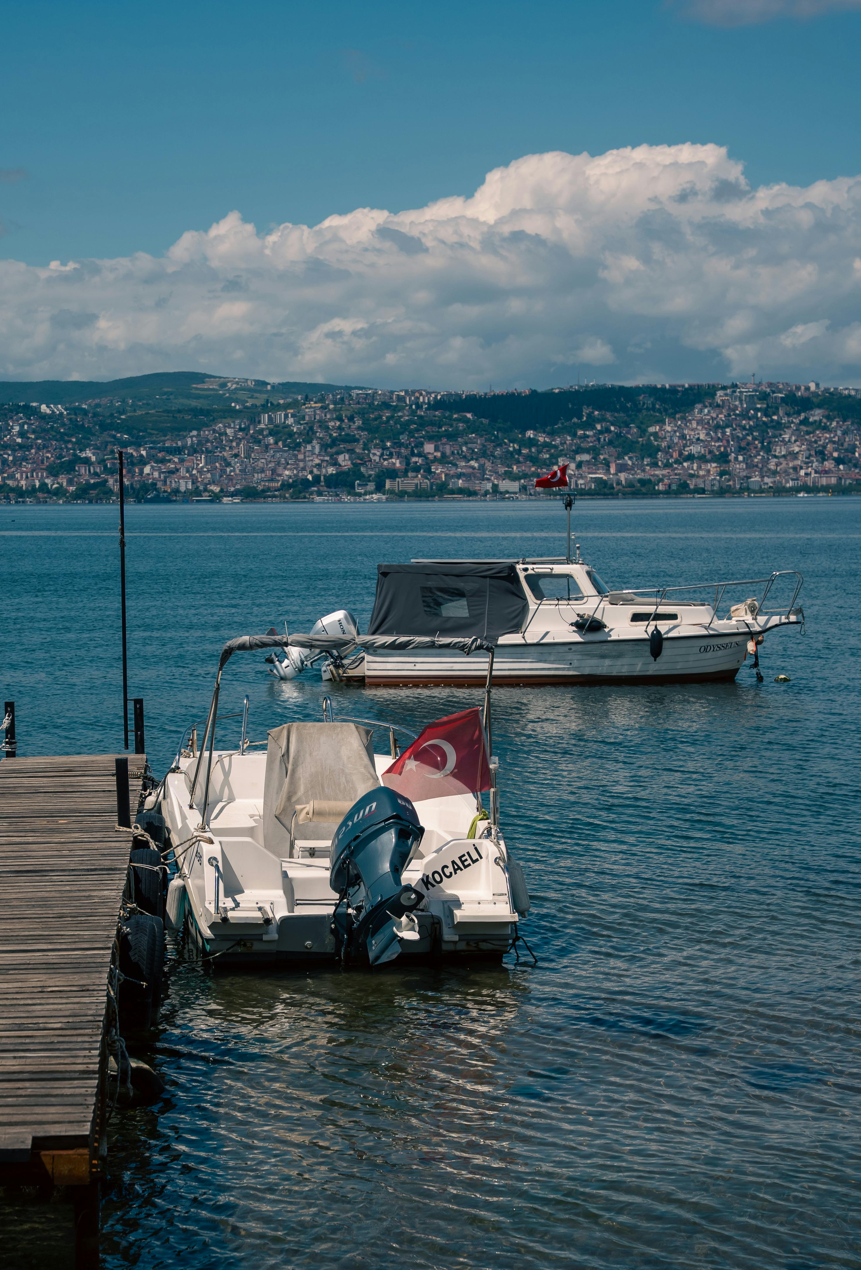 Two boats with Turkish flags docked in a scenic bay in Kocaeli, Turkey, under a clear blue sky.