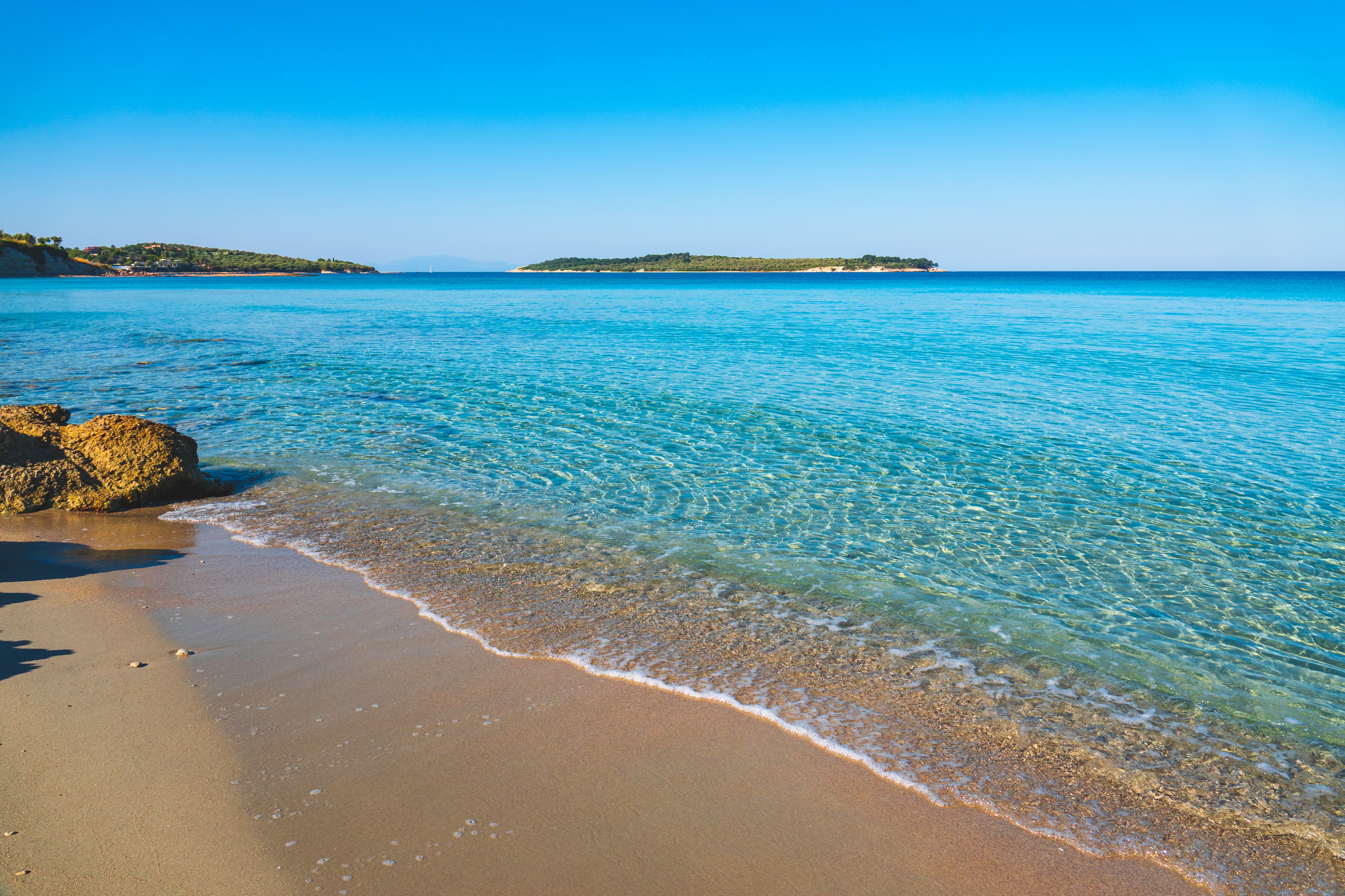 Peaceful sandy beach with crystal clear water and distant islands under a bright blue sky. - Photo by Emre Ayata on Pexels
