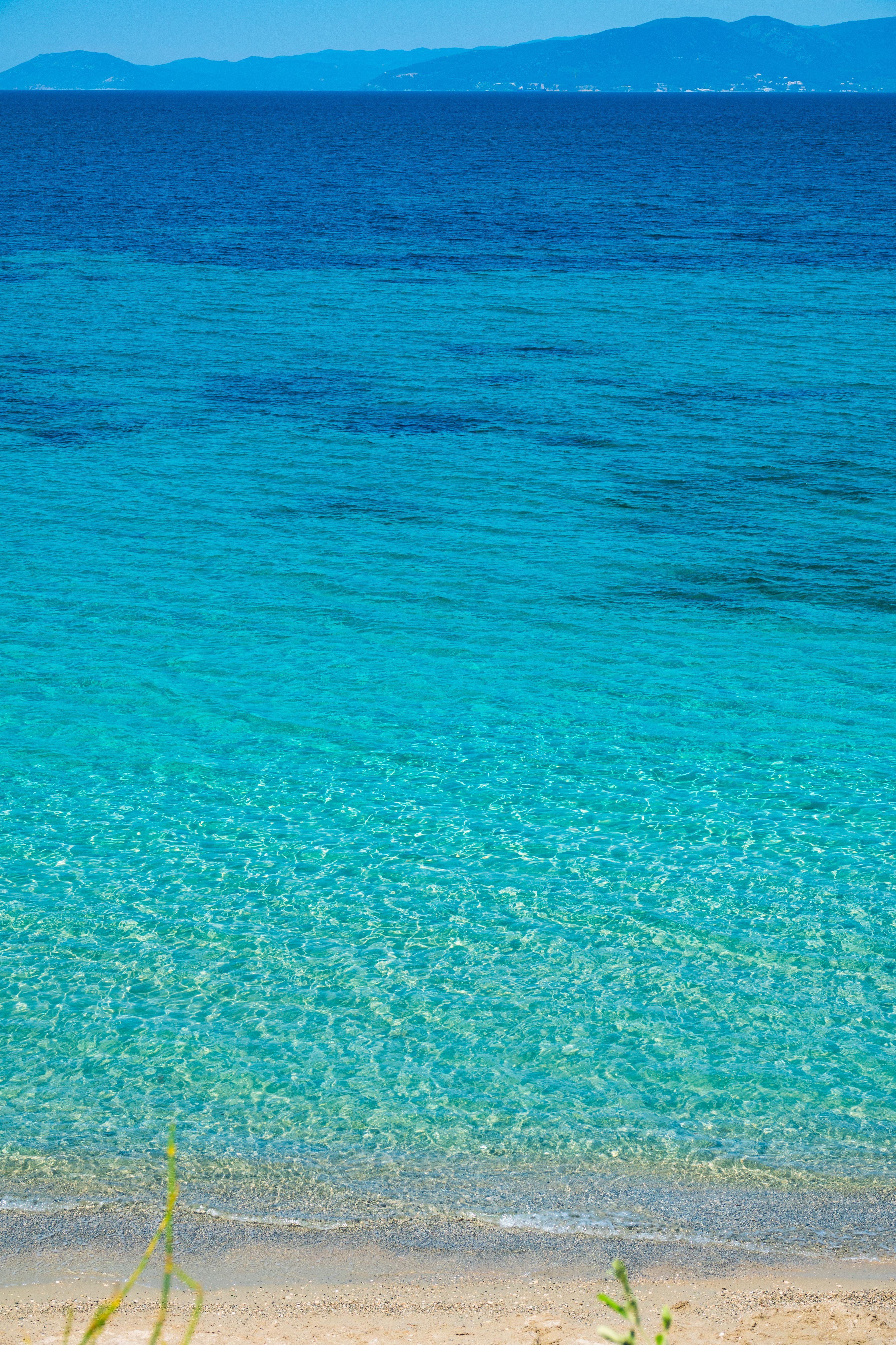 A serene beachfront with crystal clear, blue-green waters under a sunny sky.