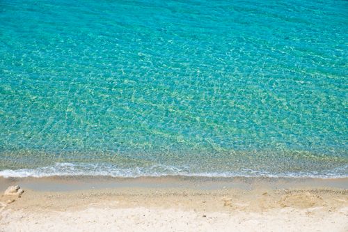 Free Pristine turquoise water gently lapping at a sandy beach under the bright sun. Stock Photo