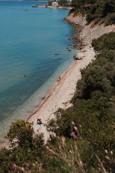 Aerial view of a serene coastal beach with people swimming and lush greenery.