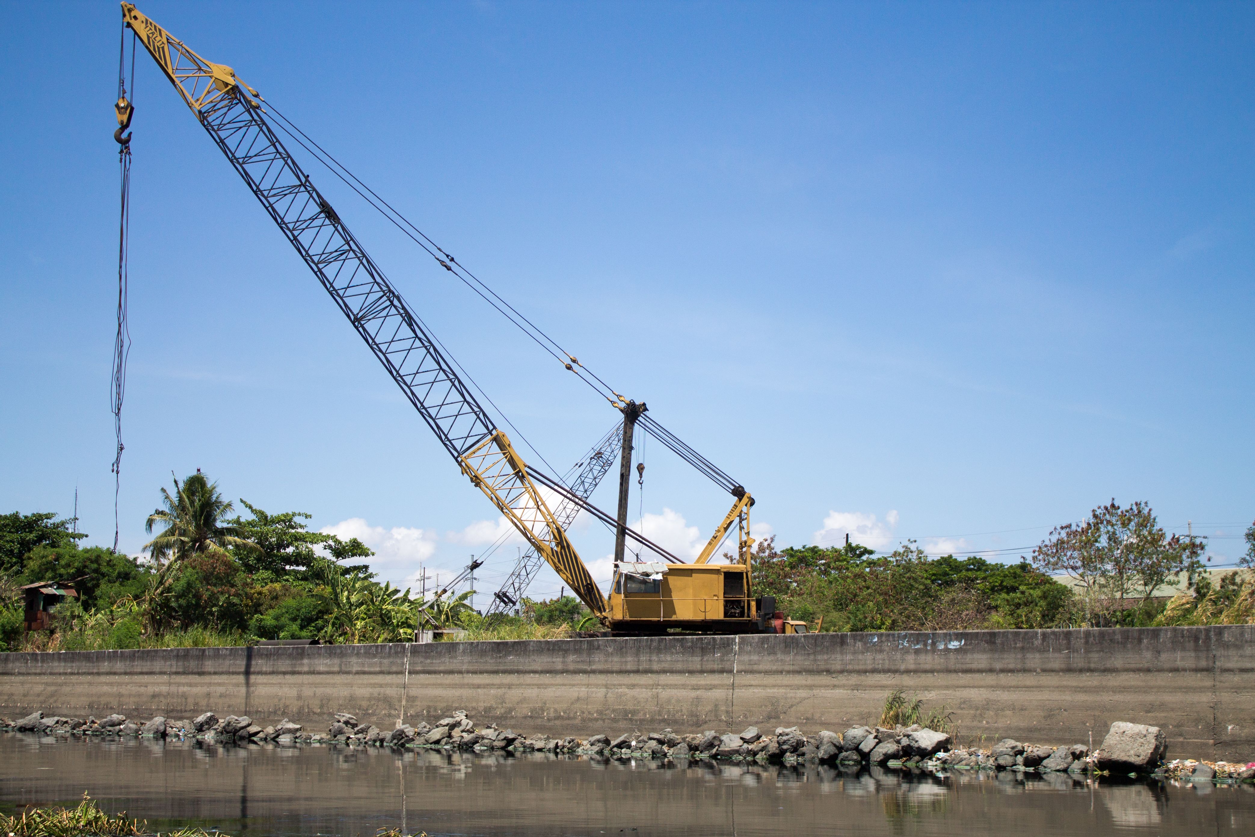 Yellow industrial crane operating in a construction area near a river.