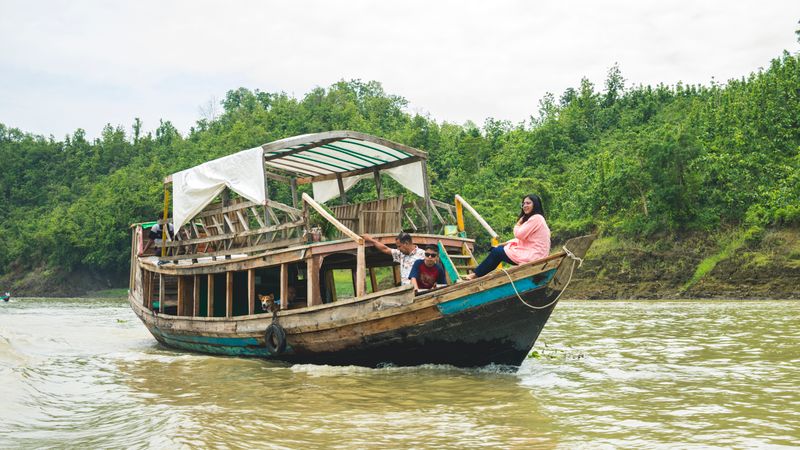 A traditional wooden boat navigates a lush river with passengers enjoying the scenic view.