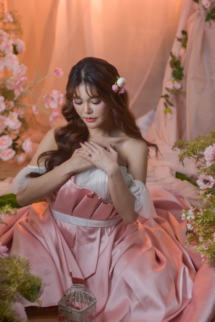 A serene woman in a pink dress surrounded by flowers, exuding elegance and tranquility.