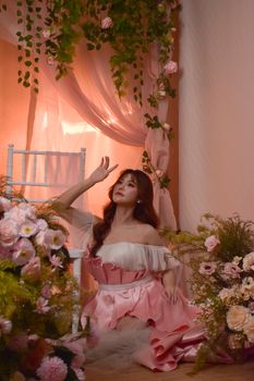Elegant woman in a floral-themed setting, wearing a pink gown, surrounded by flowers and soft lighting.