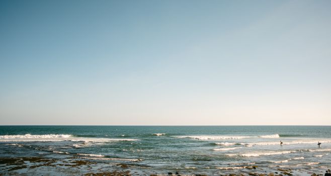 Tranquil ocean scene with surfers catching waves under a clear sky, perfect for a summer day.