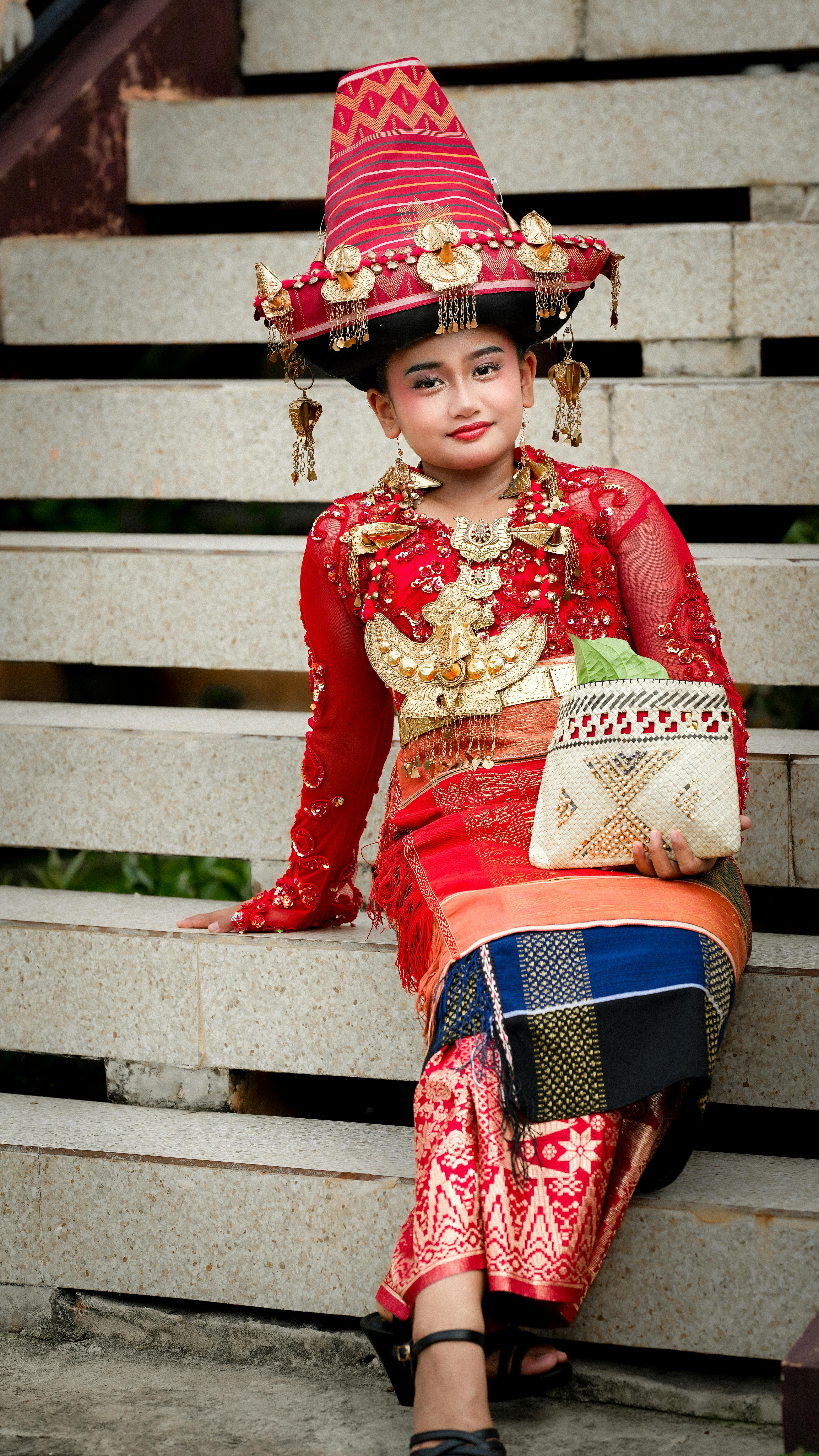 Young woman in traditional Indonesian dress with ornate jewelry, sitting on steps in Jakarta.