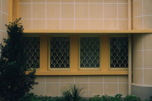 Exterior wall with art deco style windows and geometric yellow grills.