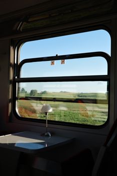 Train window view of Polish countryside with fields and hills under a clear blue sky.