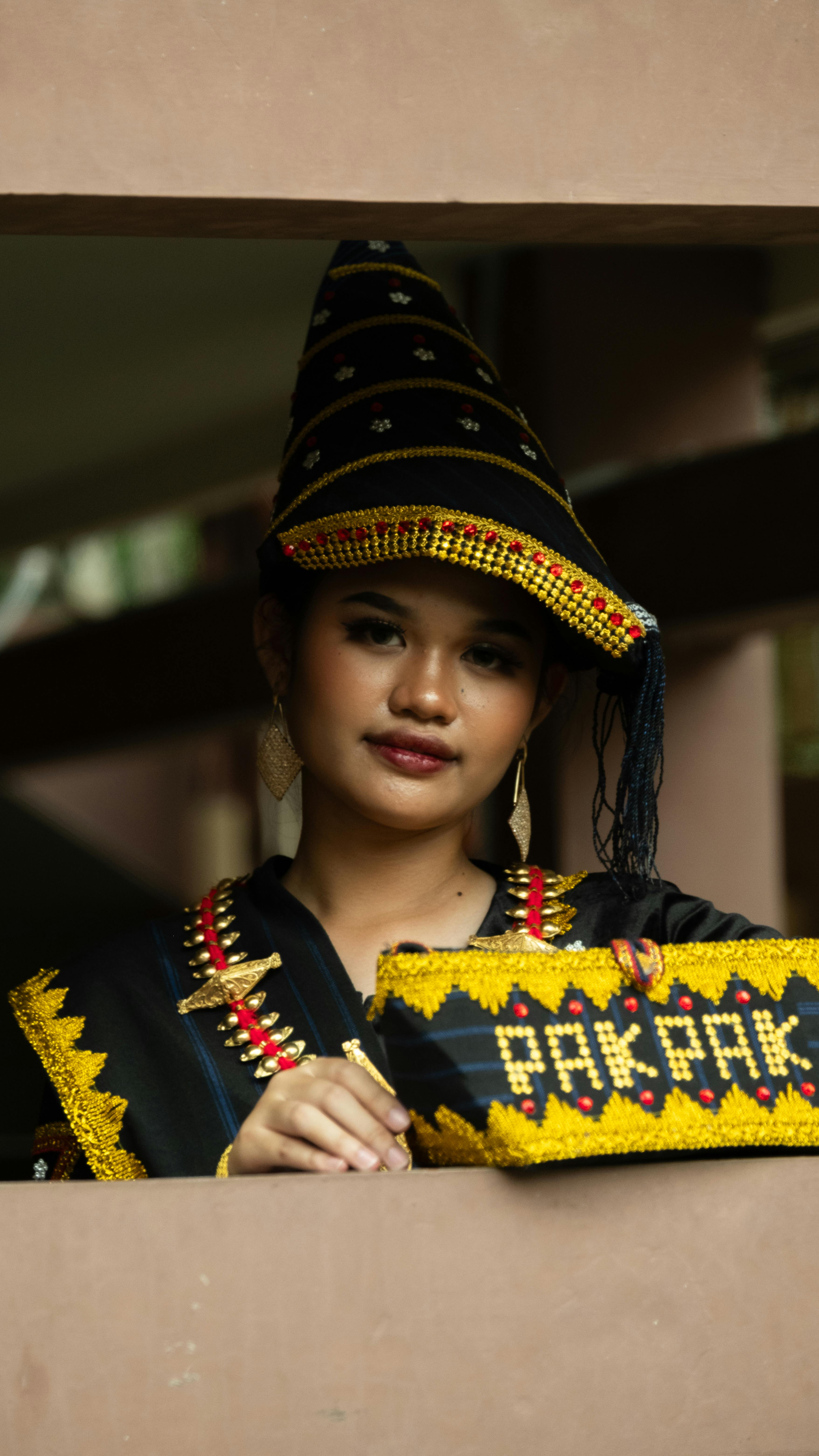 Portrait of a young woman wearing traditional Pakpak attire with cultural headpiece, indoors.