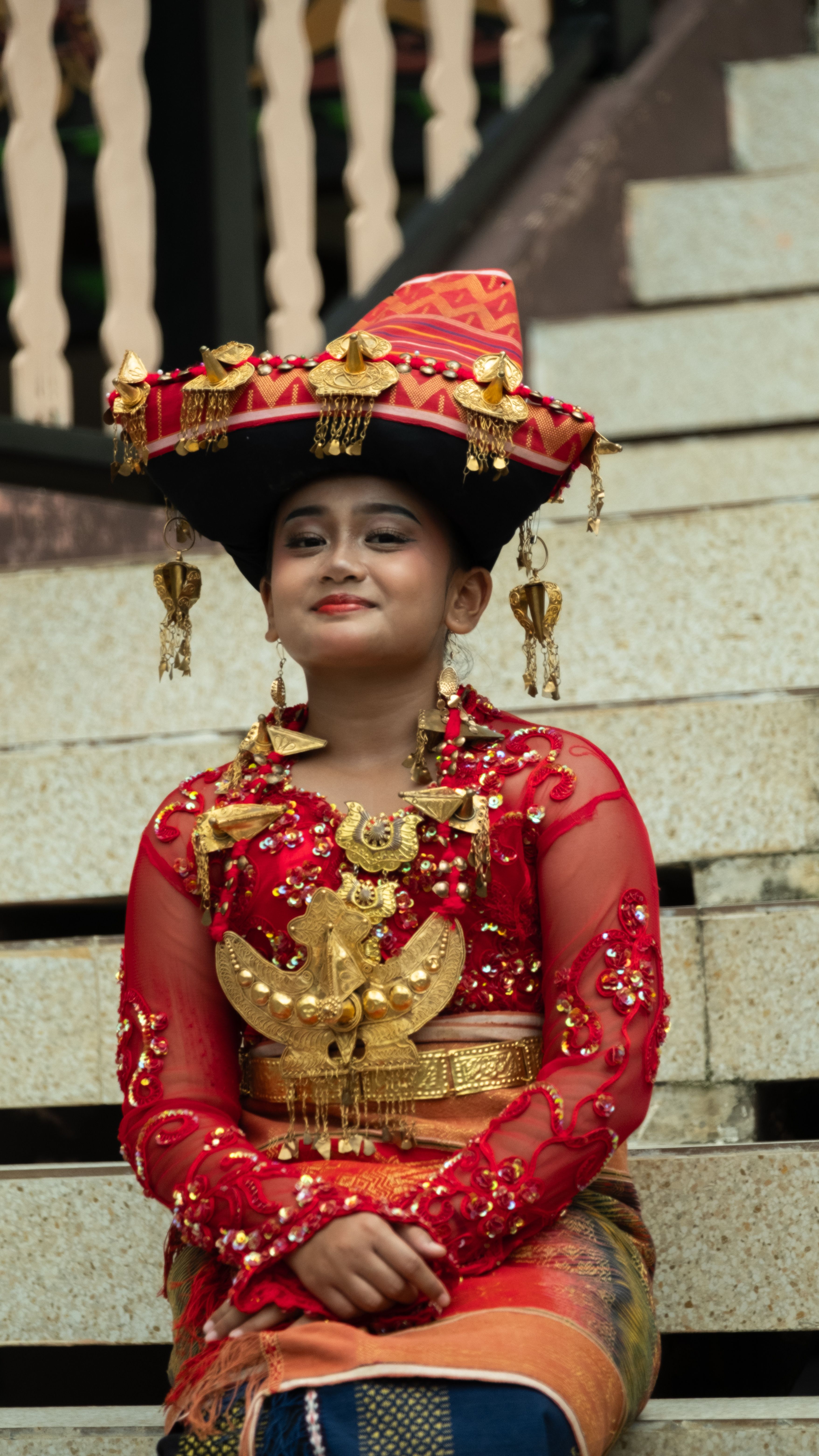 A young woman wearing vibrant traditional Batak attire sits on stairs, showcasing cultural diversity.