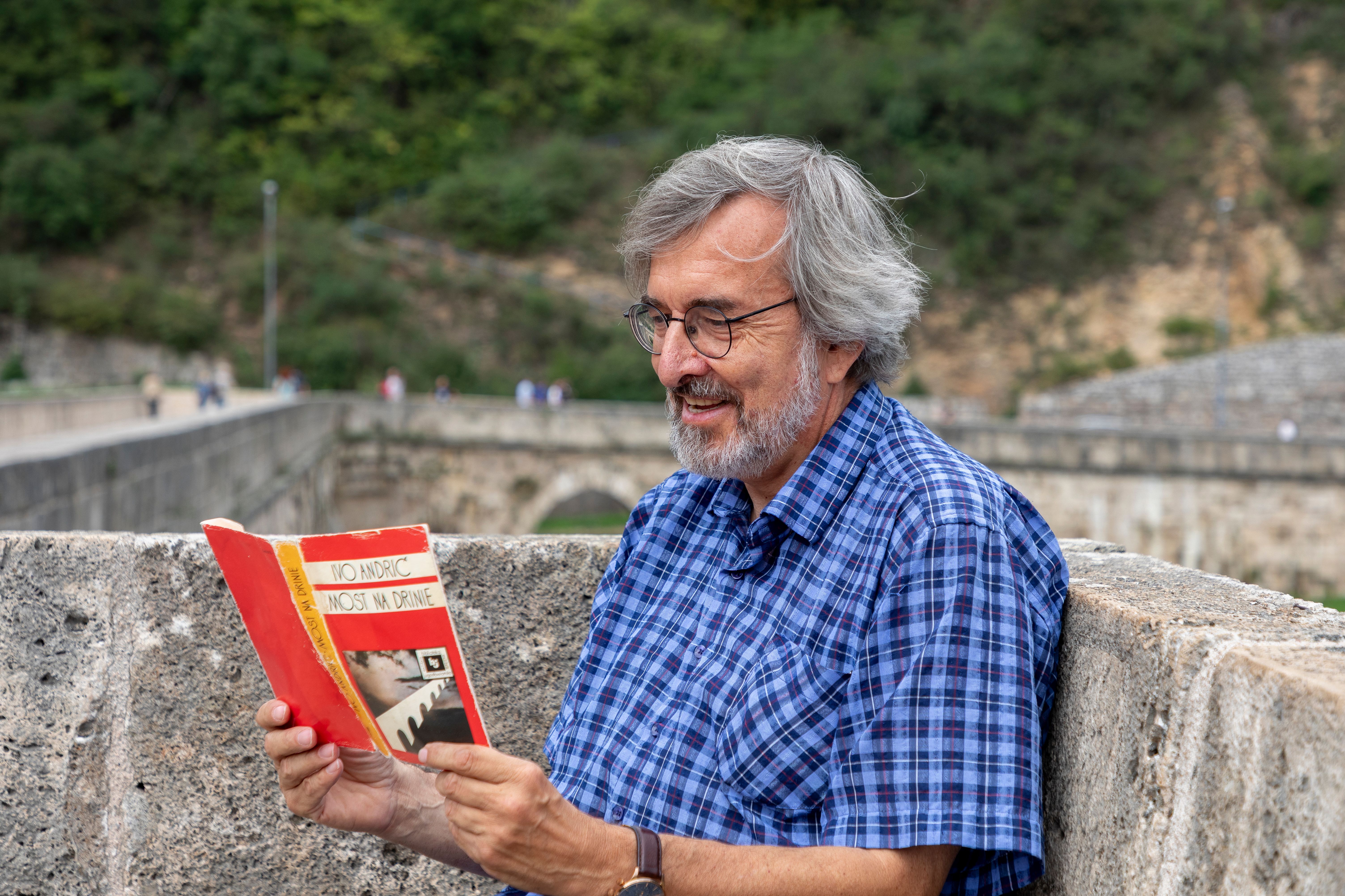 Elderly man enjoying a book on the historic Višegrad Bridge in Bosnia and Herzegovina.