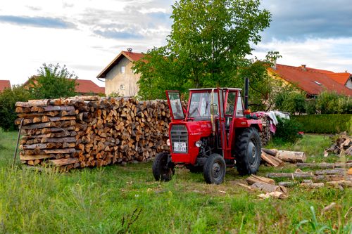 Free A red tractor beside a stacked woodpile in a rural Croatian village during the day. Stock Photo
