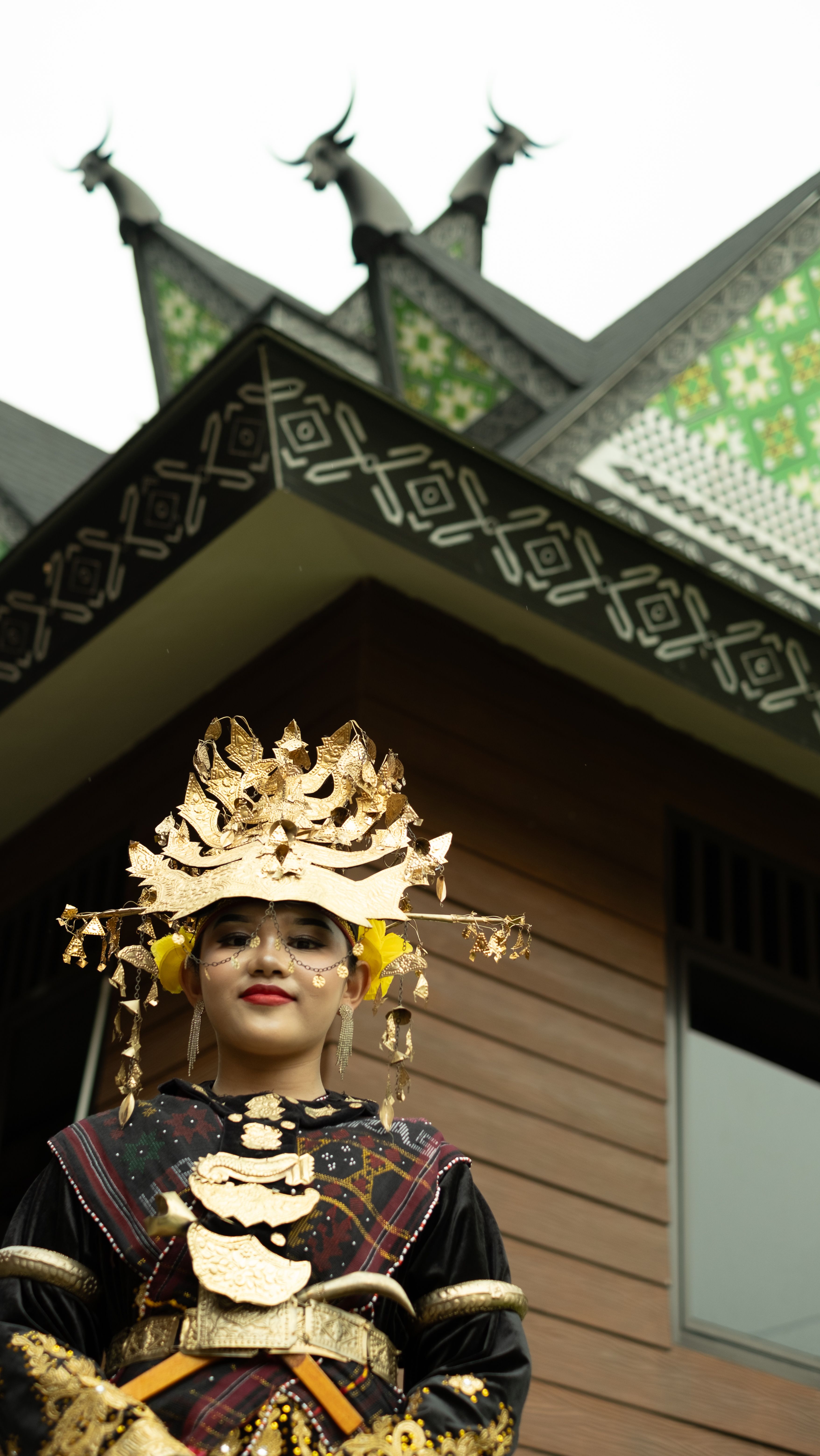 Portrait of a woman in traditional Indonesian clothing with unique architectural backdrop.