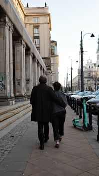 A couple enjoys a walk down a street in Warsaw, Poland, embodying urban life and togetherness.