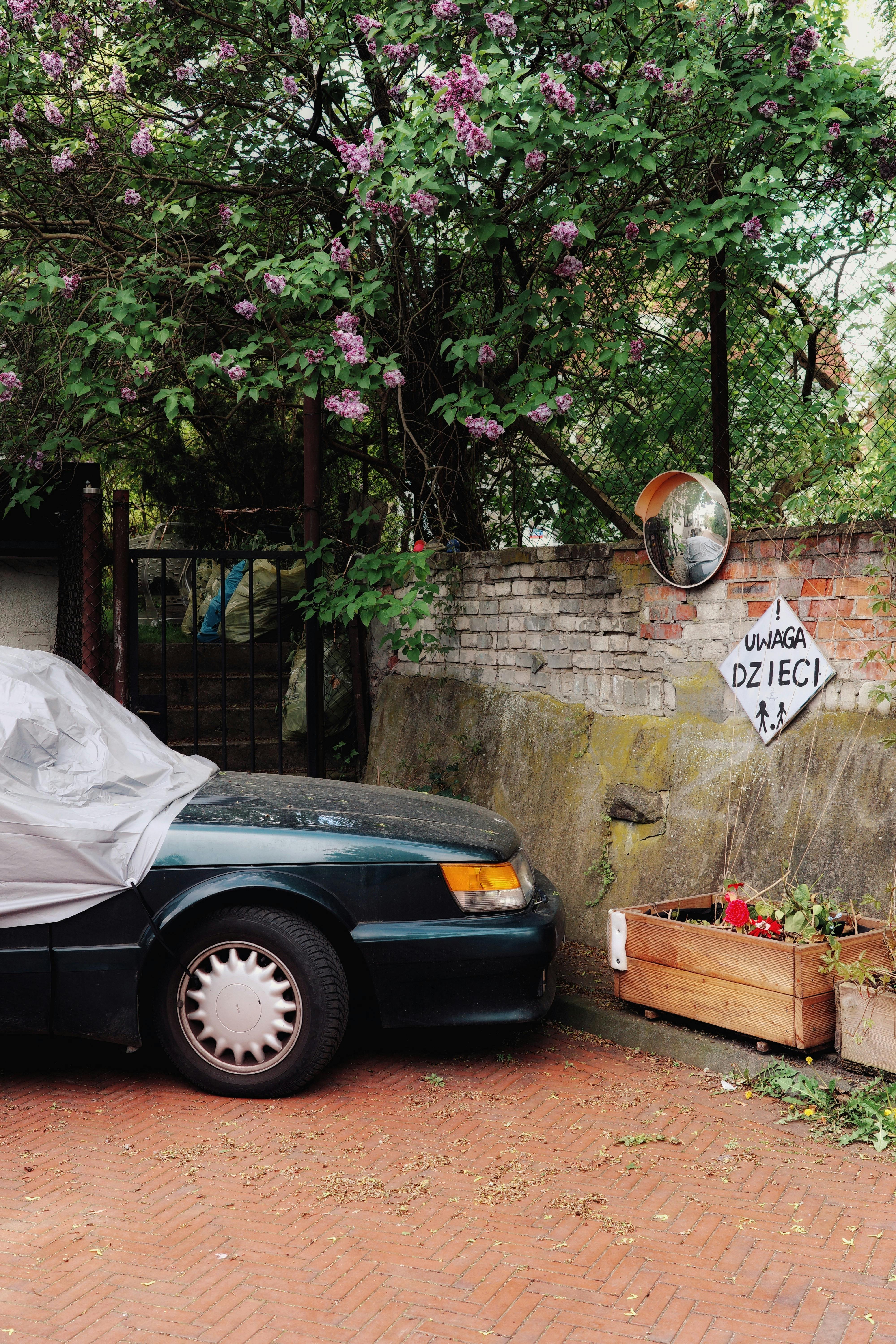 Covered car by brick wall with warning sign in Warsaw, Poland.
