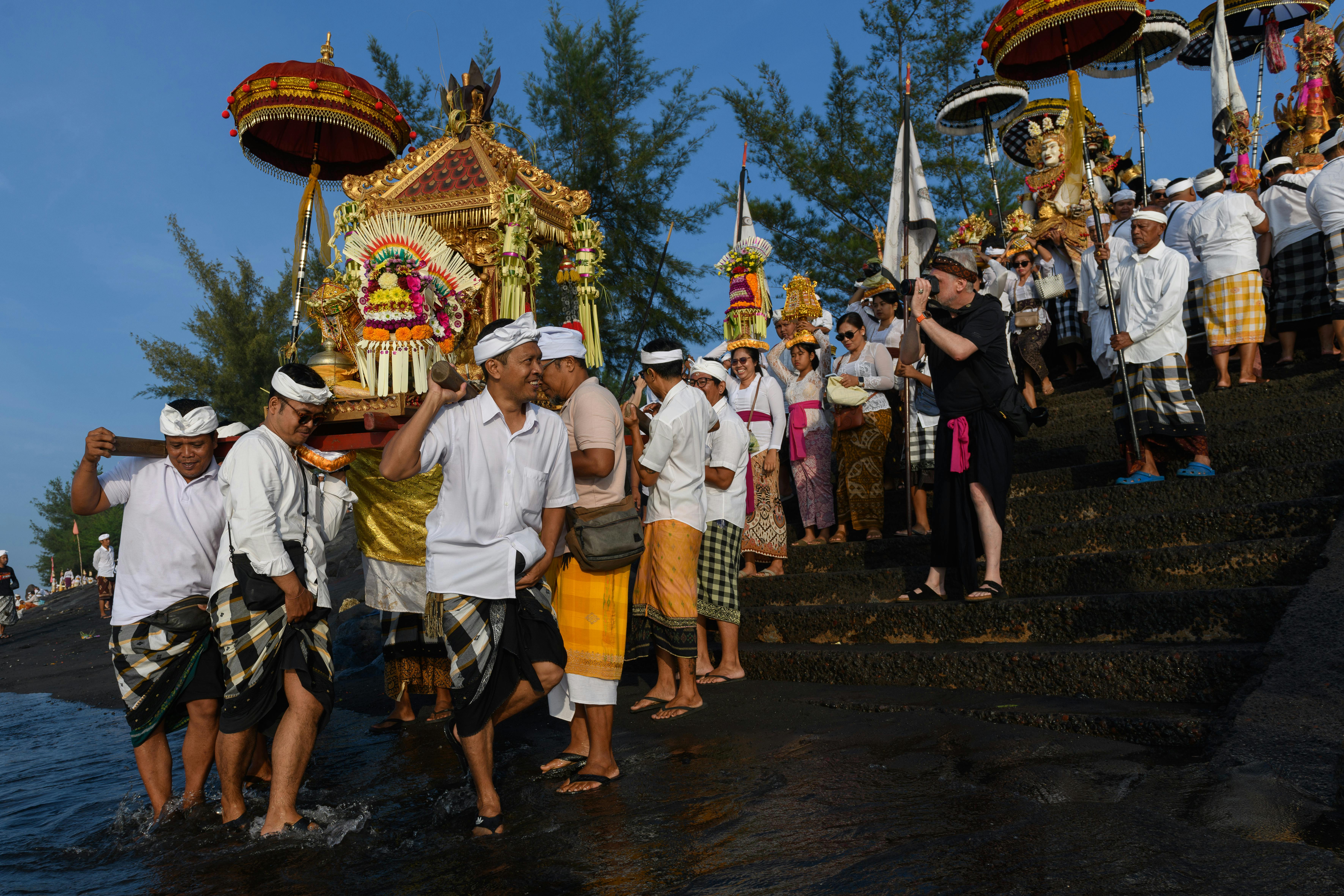 ฟรี ชาวบาหลีในชุดพื้นเมืองกำลังถือเครื่องบูชาที่ตกแต่งอย่างสวยงามในพิธีริมชายหาด คลังภาพถ่าย