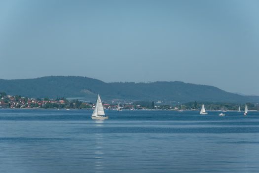 Peaceful view of a lake with sailboats and distant hills under clear blue skies.