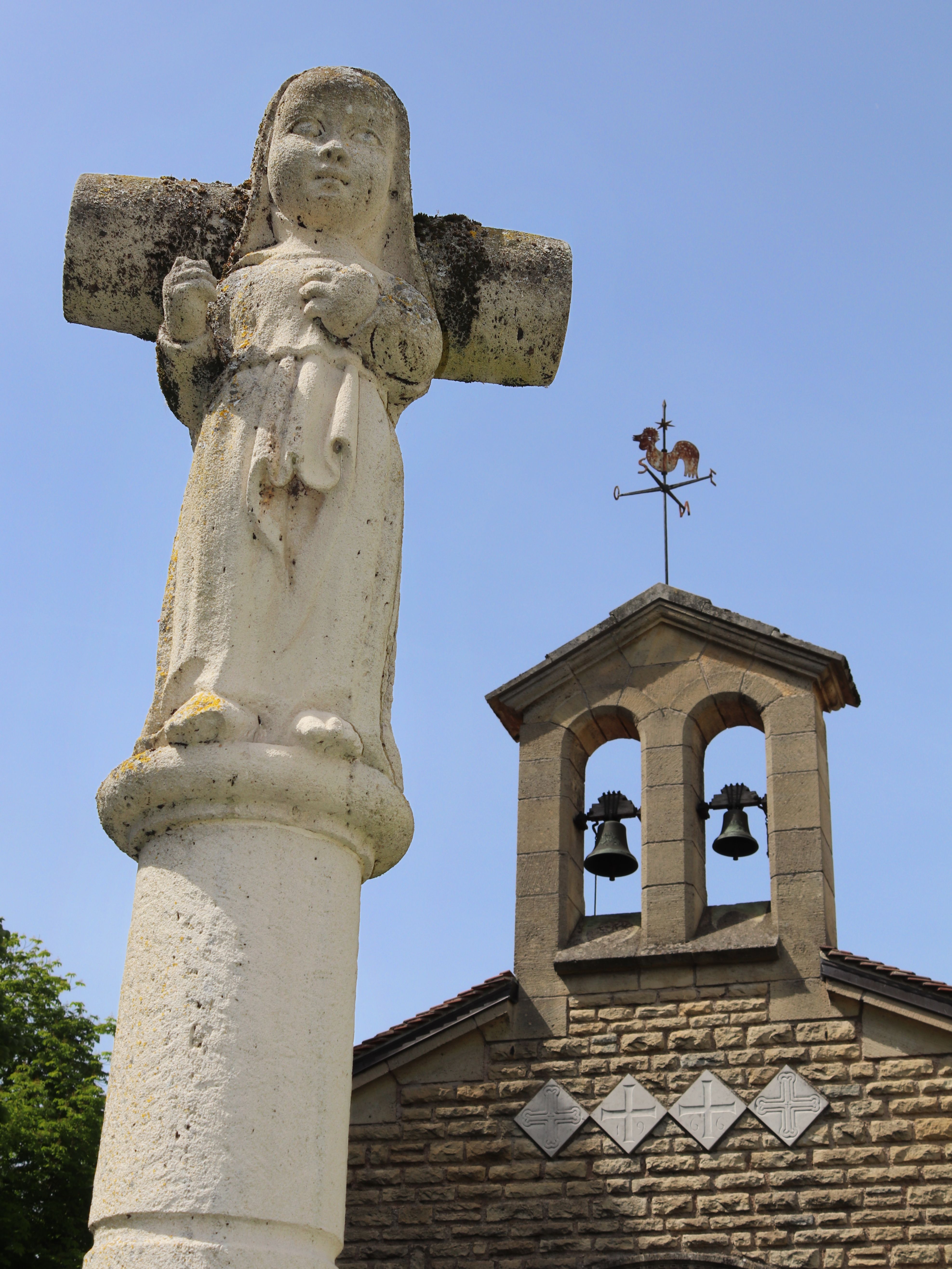 A scenic view of an ancient stone cross and a historic church bell tower under a clear blue sky.
