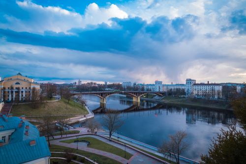 Free A serene cityscape with a bridge reflecting over a calm river under a dramatic cloudy sky at dusk. Stock Photo
