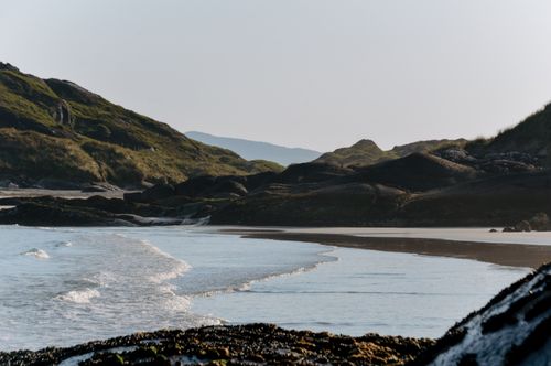 Free A serene beach scene in Ireland with rolling hills and a rocky coastline under a bright sky. Stock Photo