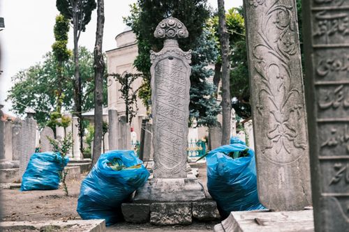Free Ancient gravestones with intricate carvings in a serene cemetery setting, blue plastic bags nearby. Stock Photo
