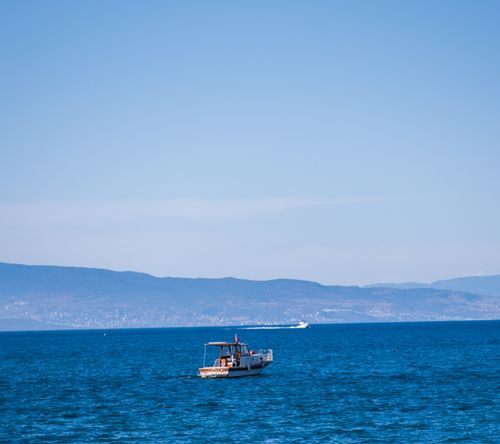 Free A small fishing boat glides across the blue Aegean Sea near Foça, İzmir, with distant hills in view. Stock Photo