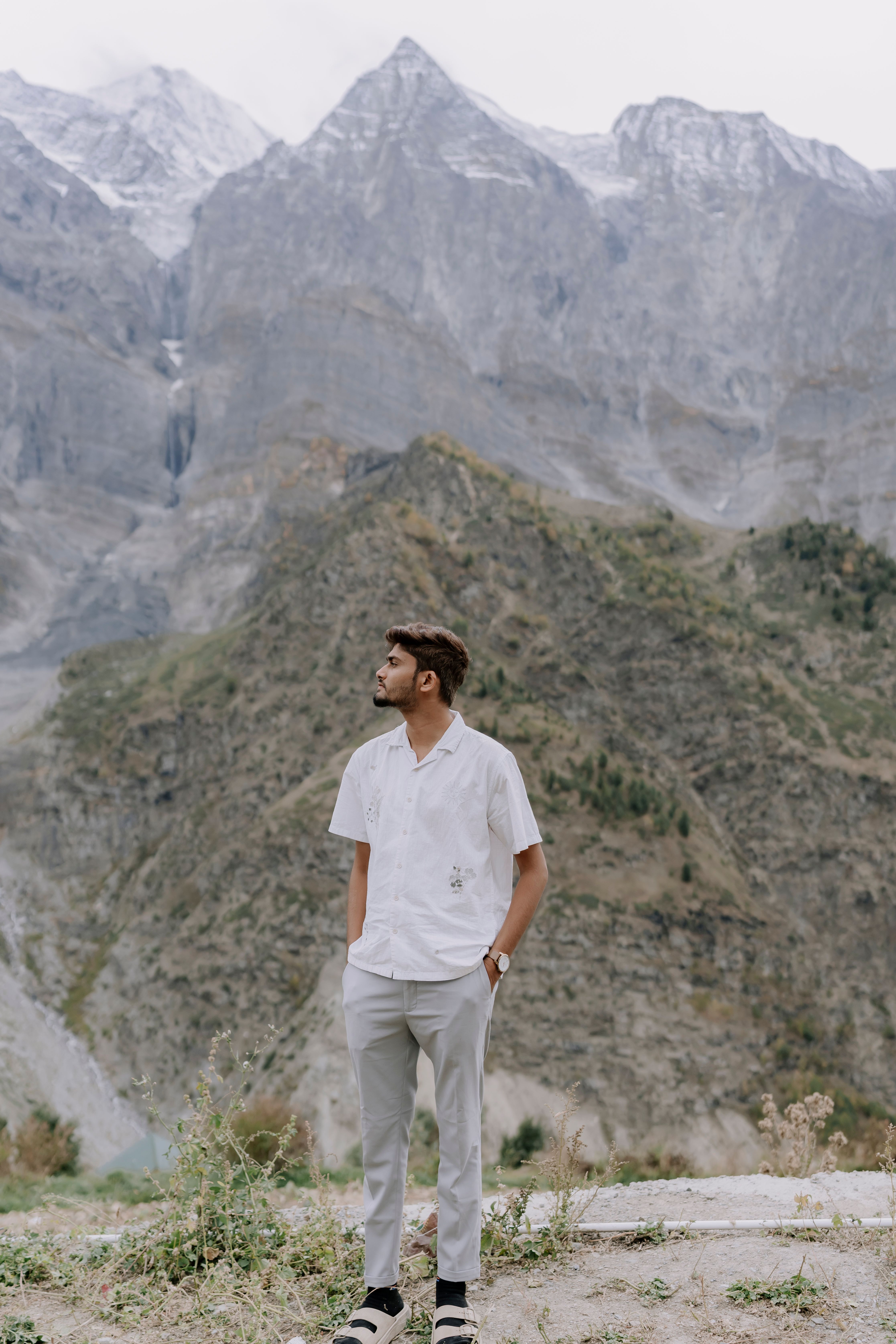 A young man stands in a serene mountain setting, looking away, conveying a sense of exploration and tranquility.