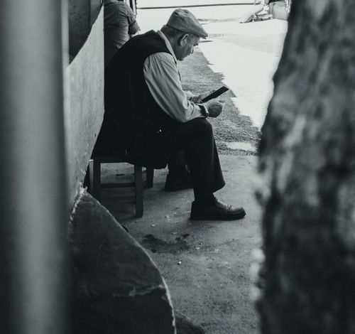 Free Black and white photo of an elderly man seated outdoors, deeply engaged in reading, conveying a peaceful moment. Stock Photo