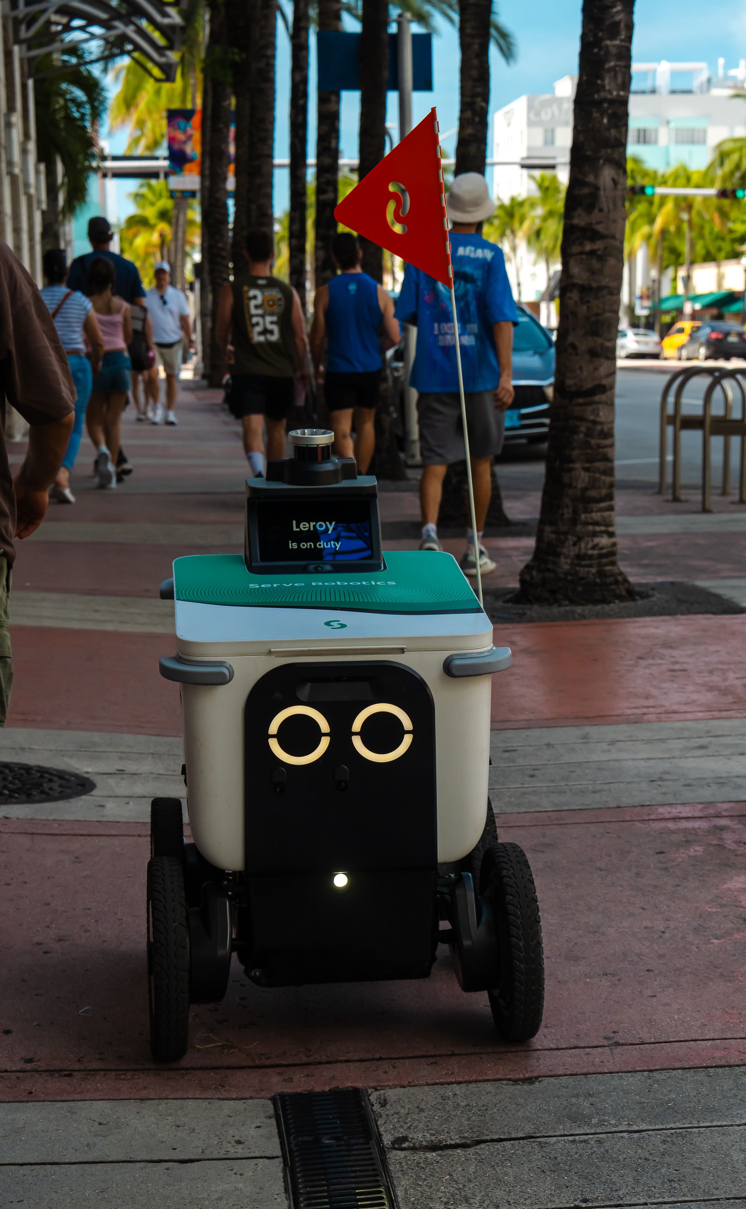 An autonomous delivery robot navigating a city street among pedestrians during the day.