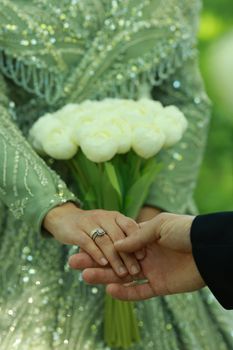 Close-up of a couple holding hands with a bouquet during a wedding ceremony.