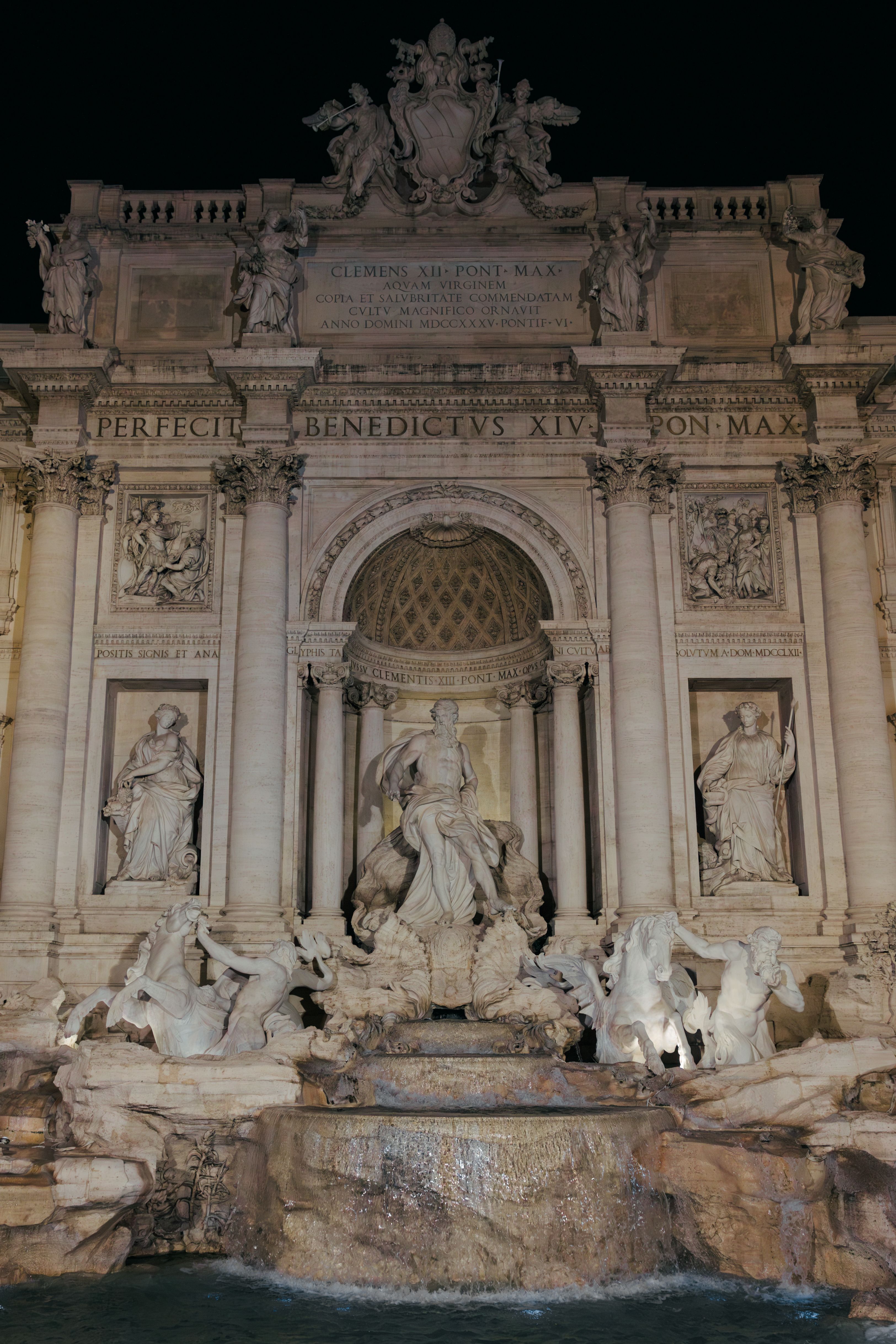 A nighttime view of the iconic Trevi Fountain in Rome, showcasing its intricate sculptures and flowing water.