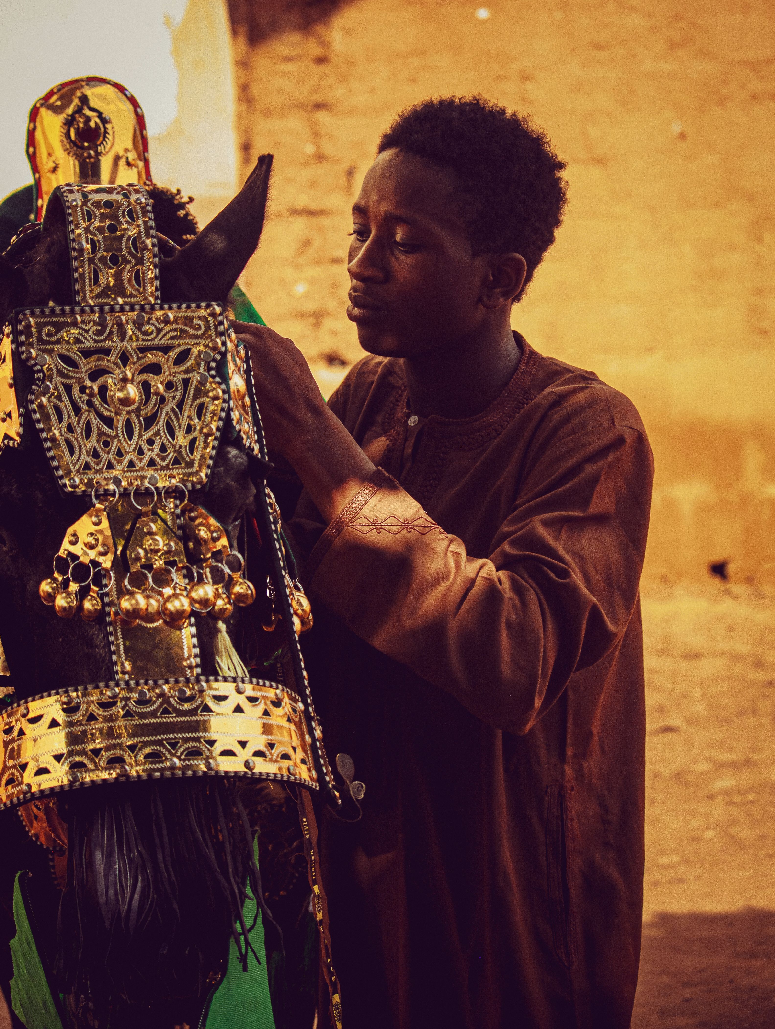 A young man in Zaria City dresses a horse in ornate ceremonial attire.