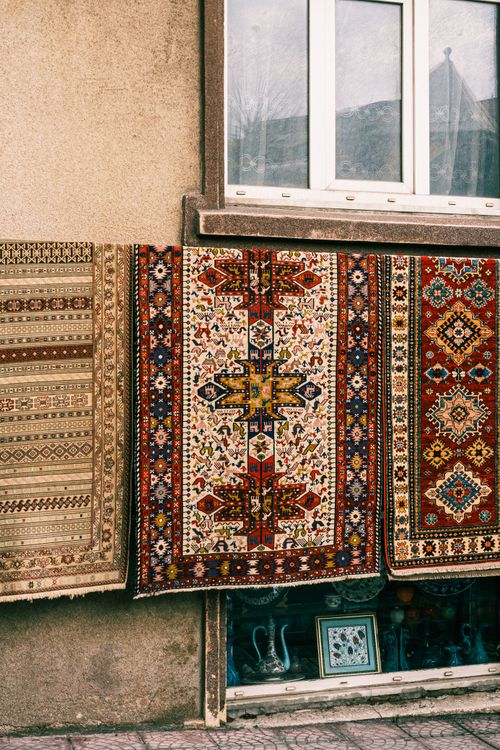 Free A vibrant display of traditional woven rugs hanging outside, showcasing intricate patterns and textures. Stock Photo
