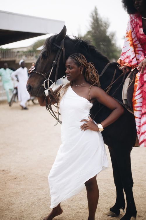 Free Stylish woman in white dress posing beside horse, showcasing confidence and elegance. Stock Photo