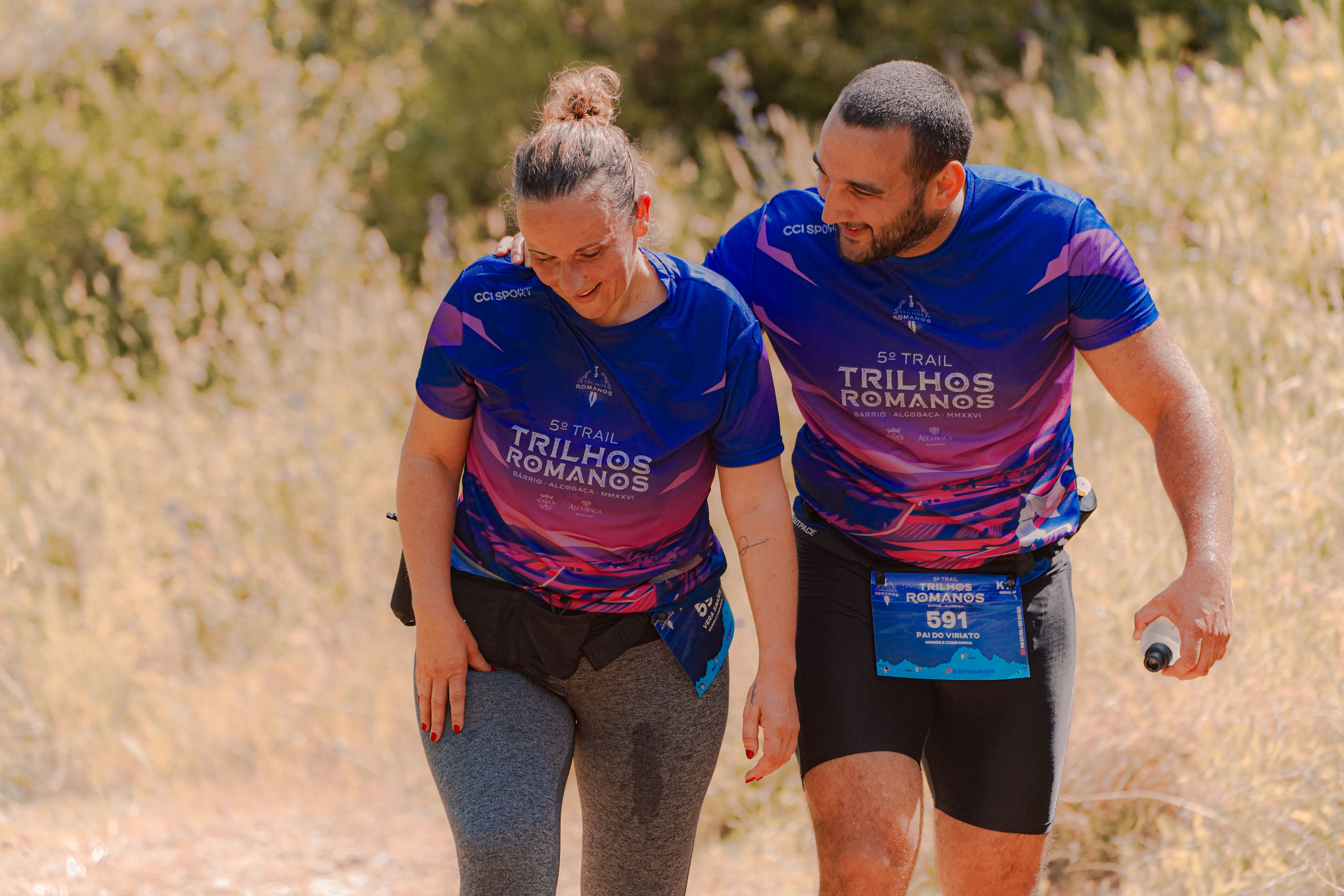 Two trail runners share a moment of encouragement during a challenging race on a scenic Roman path.