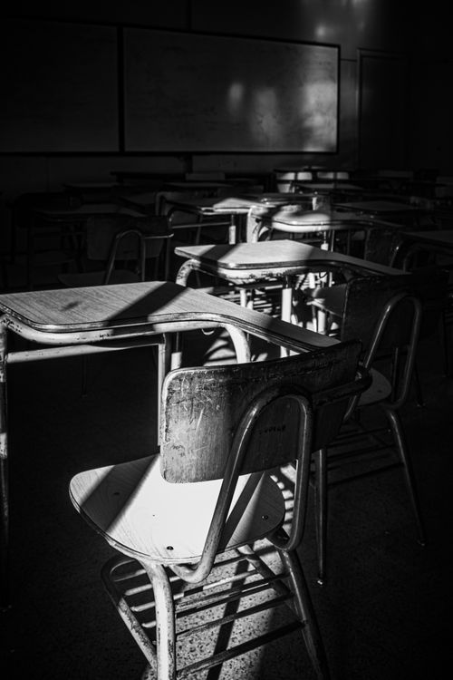 Free Black and white photo of a sunlit empty classroom with vintage desks and chairs. Stock Photo