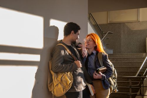 Free Two college students chatting casually by the stairs in Buenos Aires, warm lighting enhances the friendly atmosphere. Stock Photo