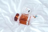 柔软的白色织物上，豪华香水瓶与珍珠项链共同营造出一种优雅而芬芳的审美意境
