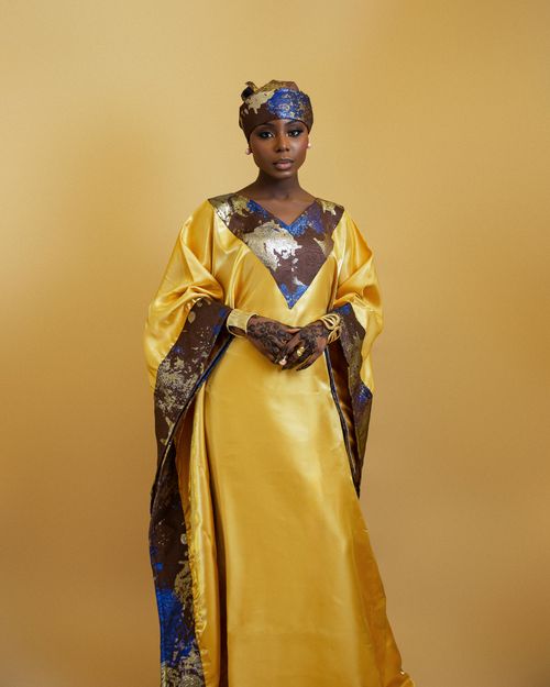 Free Portrait of a Nigerian woman in golden traditional attire against a matching background. Stock Photo