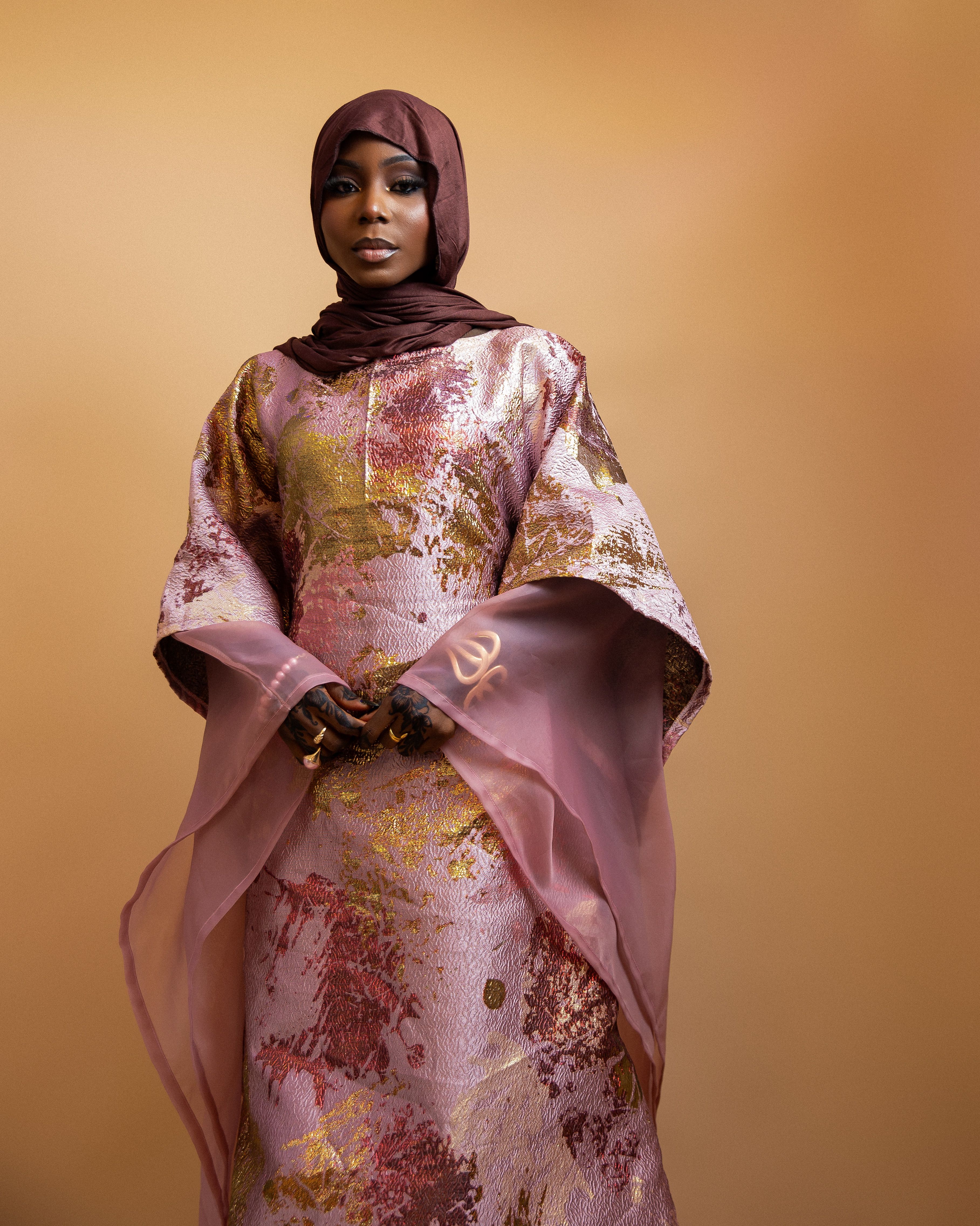 Portrait of a woman in traditional Nigerian attire with a hijab, set against a warm background.