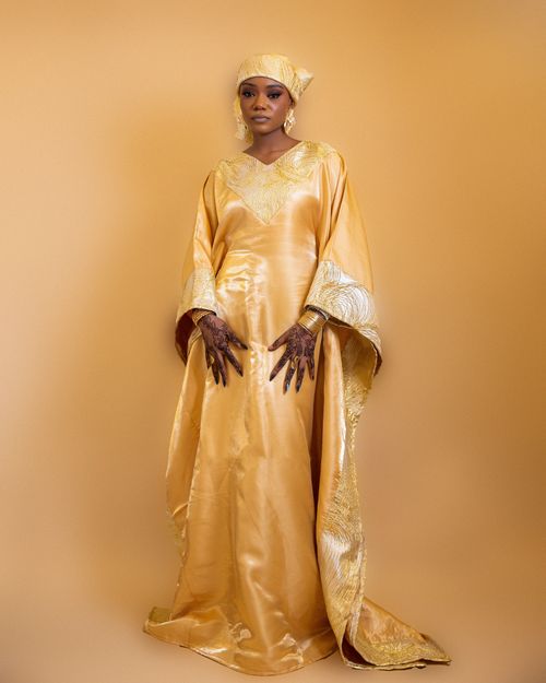 Free African woman wearing golden traditional attire with henna, posing elegantly against a matching background. Stock Photo