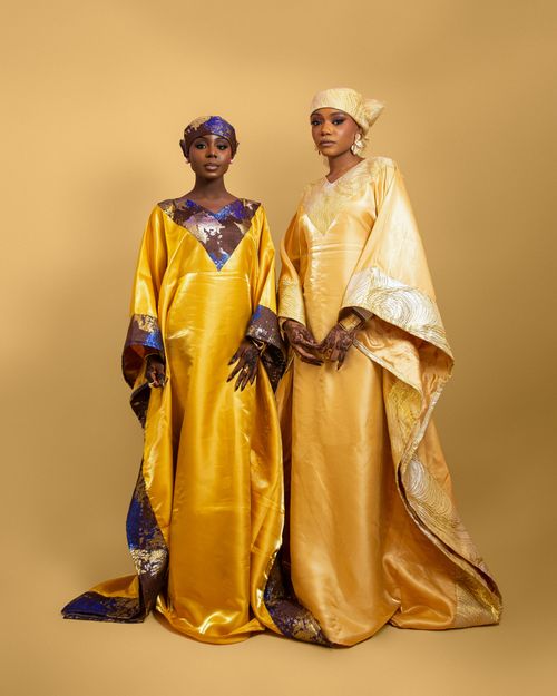 Free Two women in vibrant traditional Nigerian gowns posing elegantly on a golden backdrop. Stock Photo