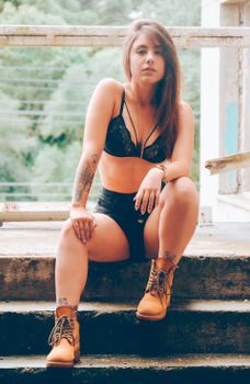 A confident young woman poses stylishly outdoors, showcasing tattoos and urban fashion.