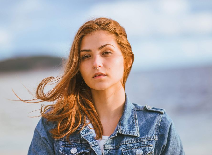 Casual outdoor portrait of woman with red hair and denim jacket by the ocean