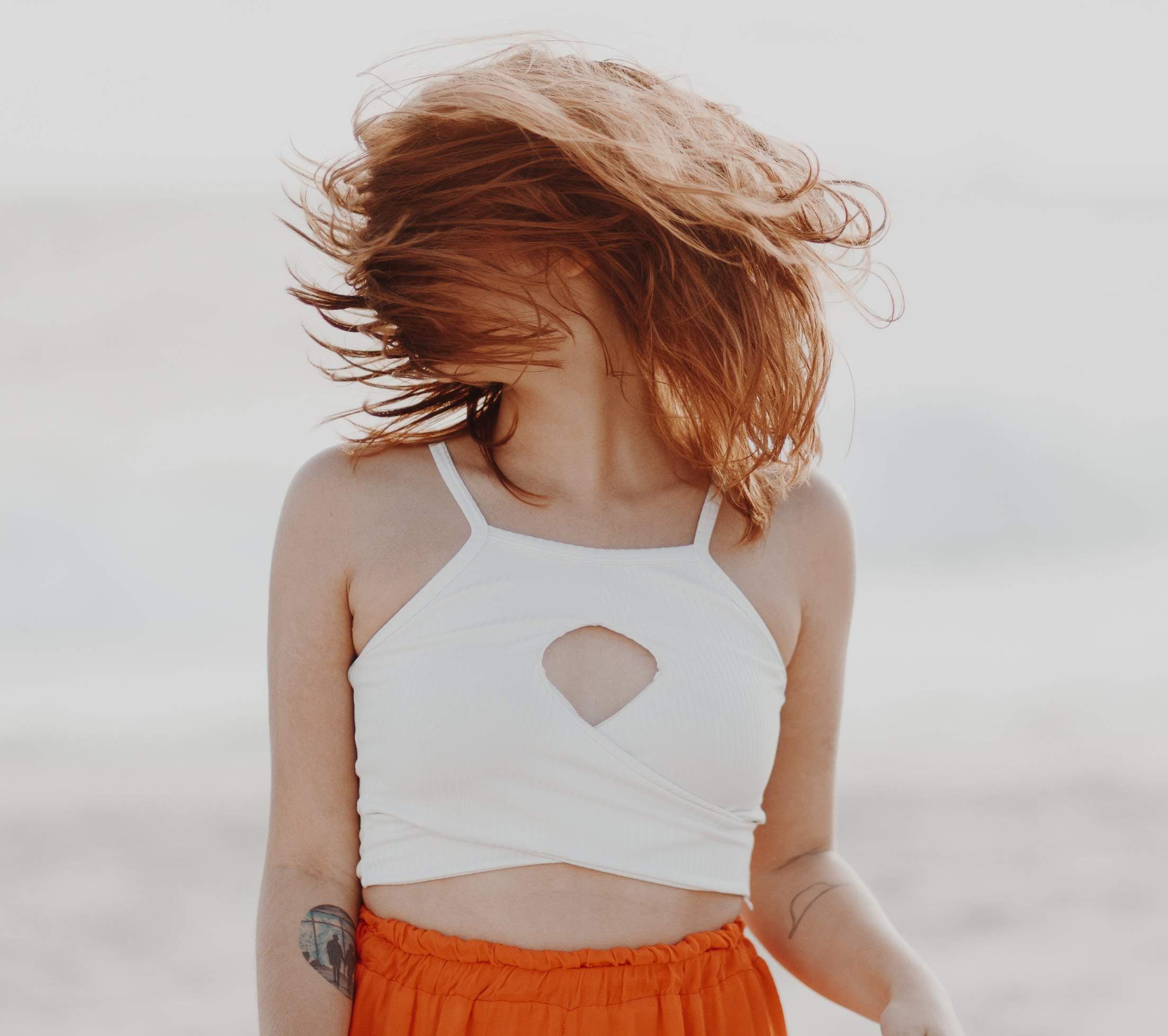 A young woman with vibrant hair enjoying the breeze at the beach, wearing a stylish summer outfit.